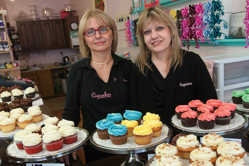 Owners, Anne Campagna and Marilyn Gouchie, in front of their well-lit cupcake display at their shop after participating in our Small Business Lighting program.