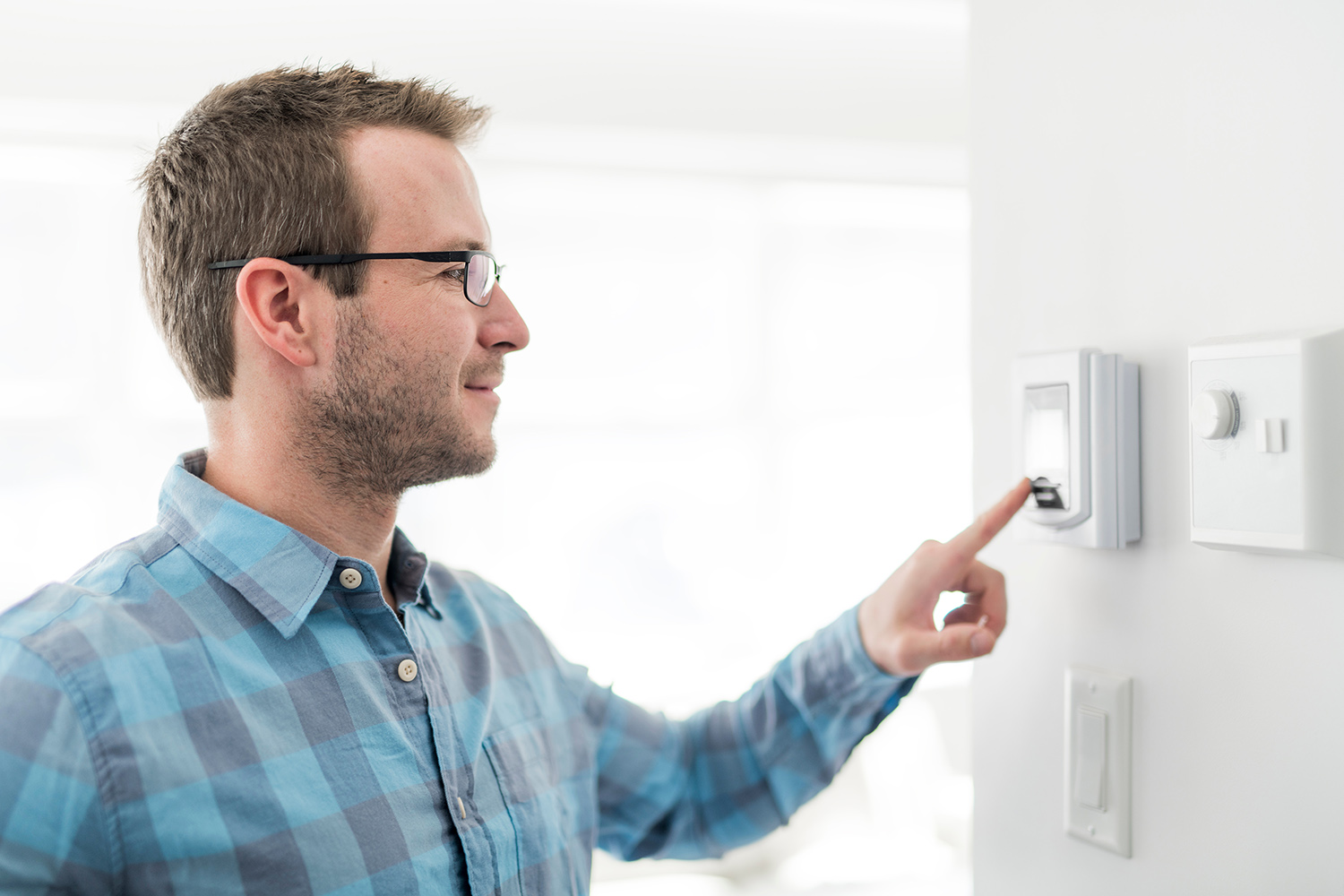 Man adjusting his smart thermostat on an interior wall of his home