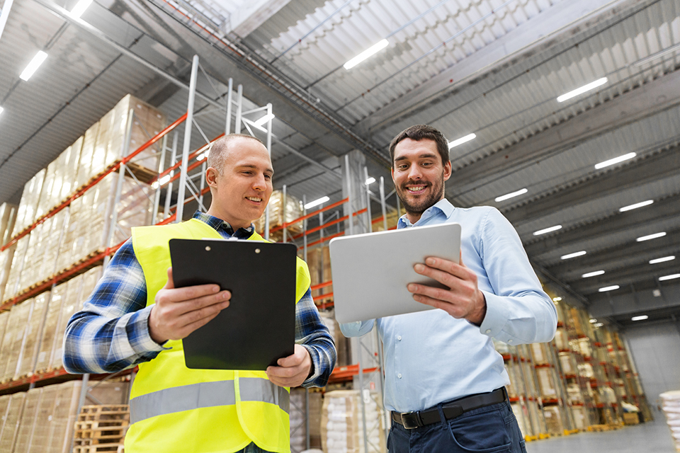 warehouse worker with clipboard talking to businessman with tablet